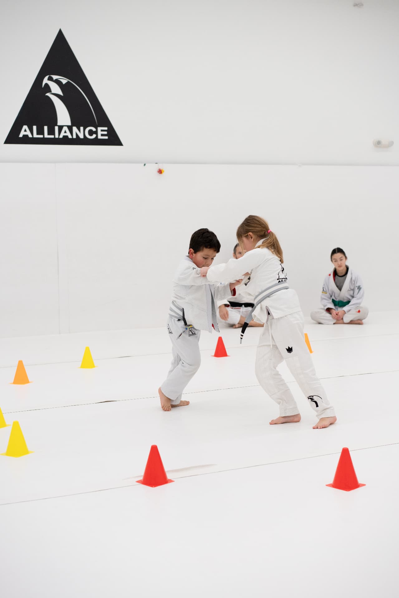 Two kids in white gis training grips on the Alliance mats